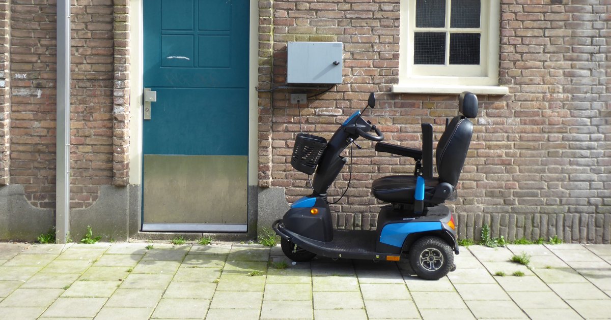 A blue four-wheel mobility scooter parked on a paved path outside a brick house