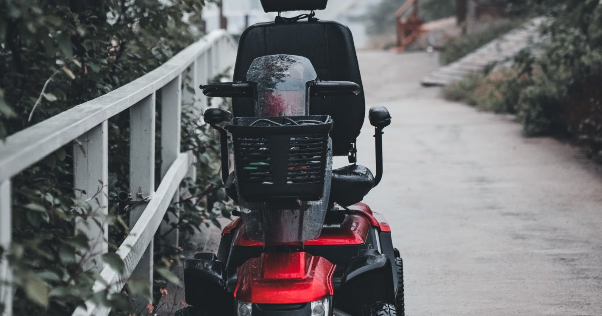 A red four-wheel mobility scooter parked on a wet village path