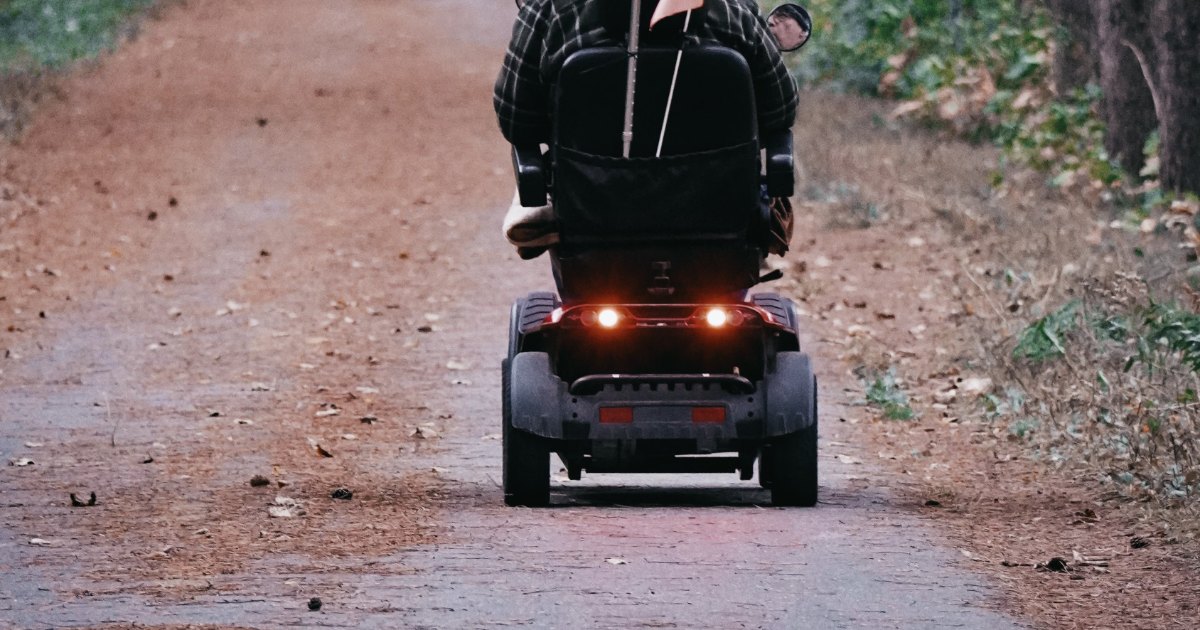 A person riding a mobility scooter along a woodland path
