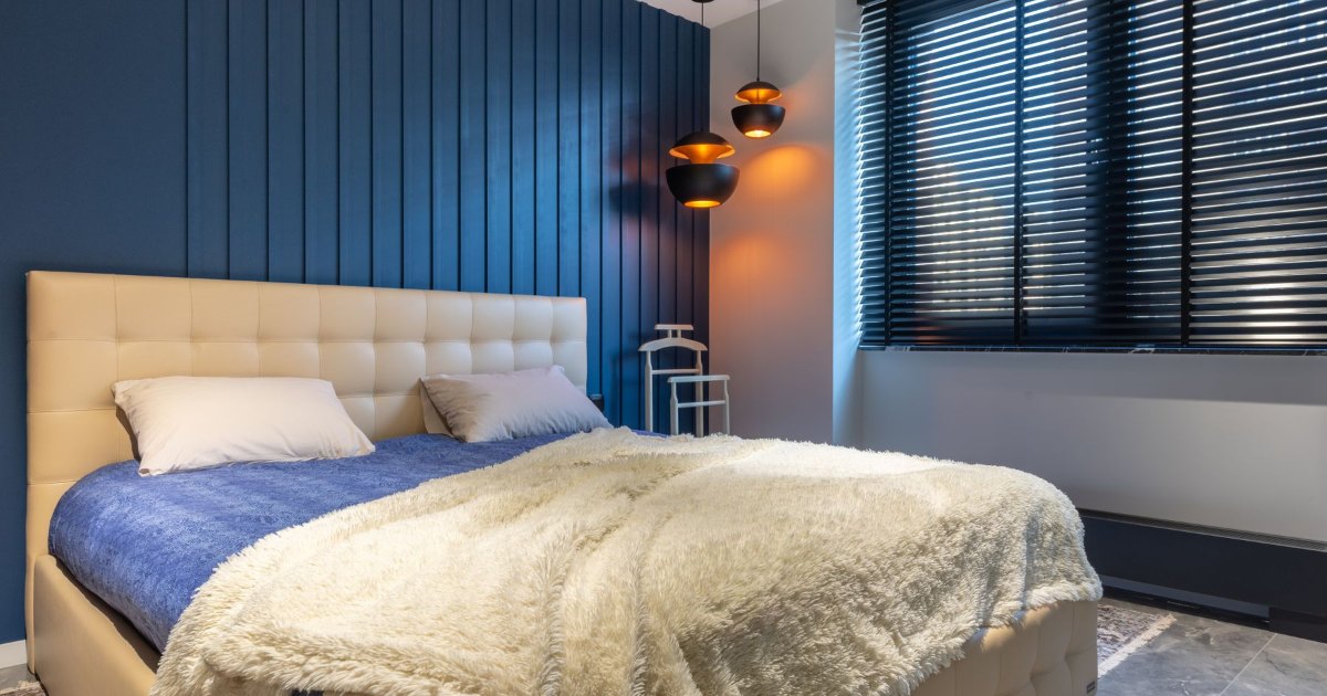A double bed with an upholstered headboard and throw in a modern bedroom with blue panelled walls