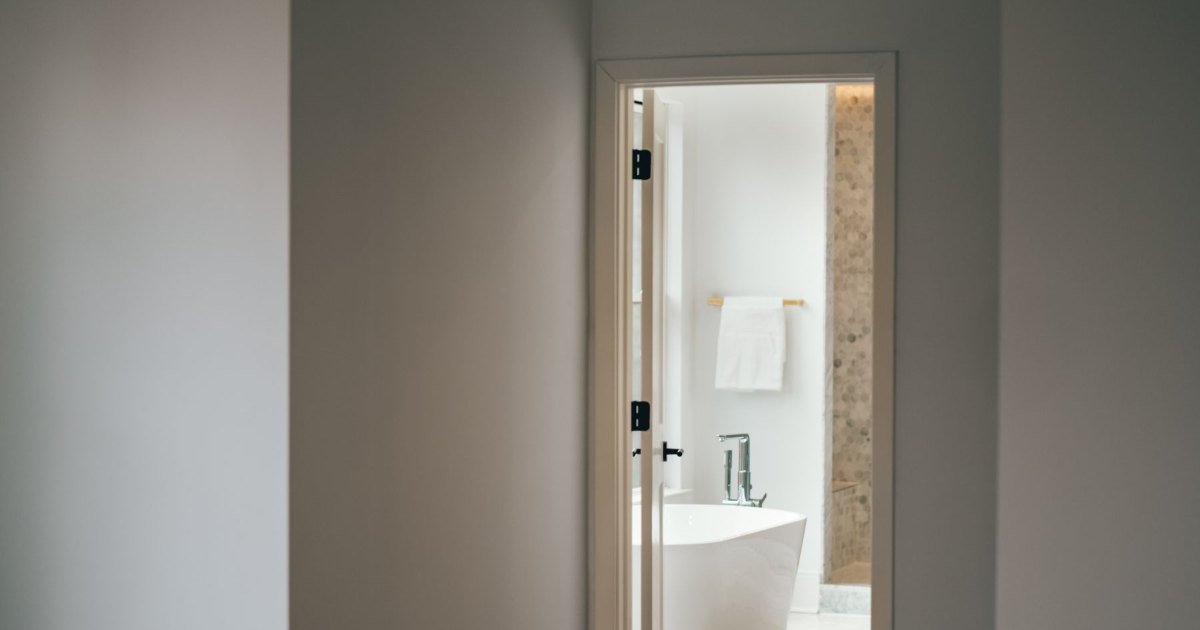 An open doorway looking through into a plain, neutral bathroom