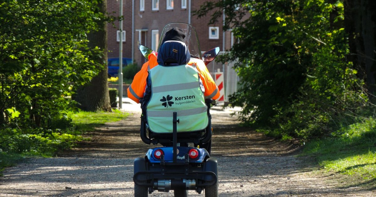 A person riding a mobility scooter along a park path, seen from behind