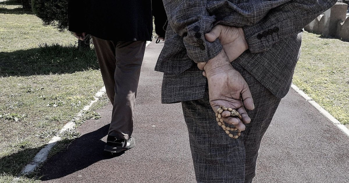An older person walking with their hands clasped behind their back