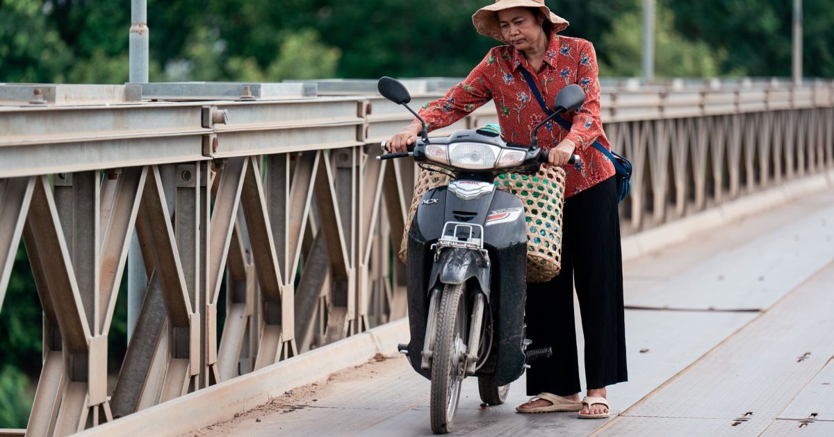 A person riding a mobility scooter across a bridge, seen from behind