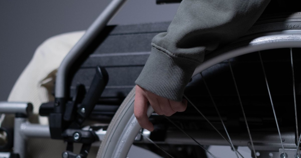 A close view of a hand resting on the push rim of a wheelchair