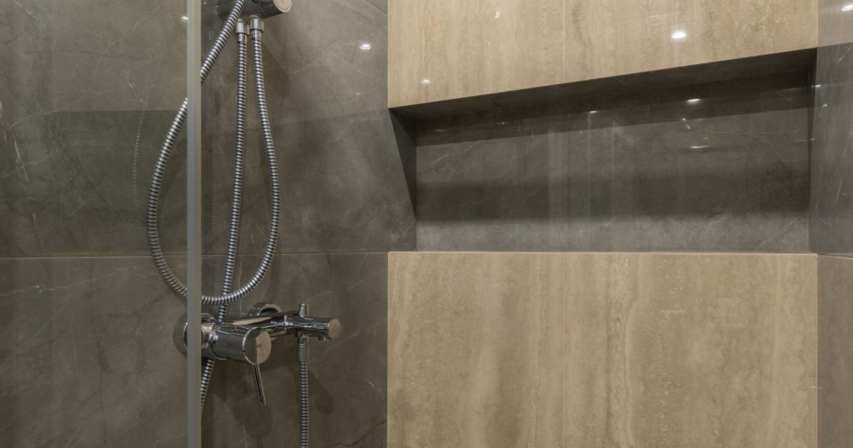 A tiled walk-in shower with a recessed shelf and glass screen