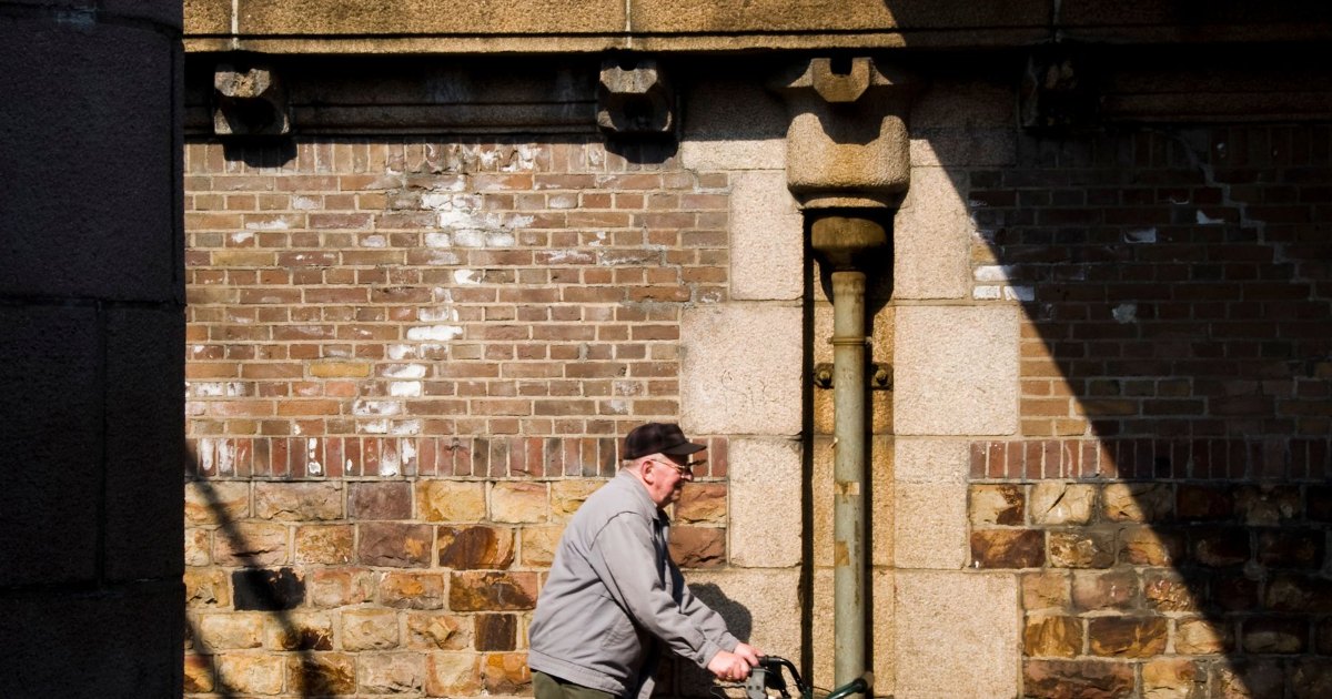 Walking frame on a pavement A person using a wheeled walking frame along a city pavement