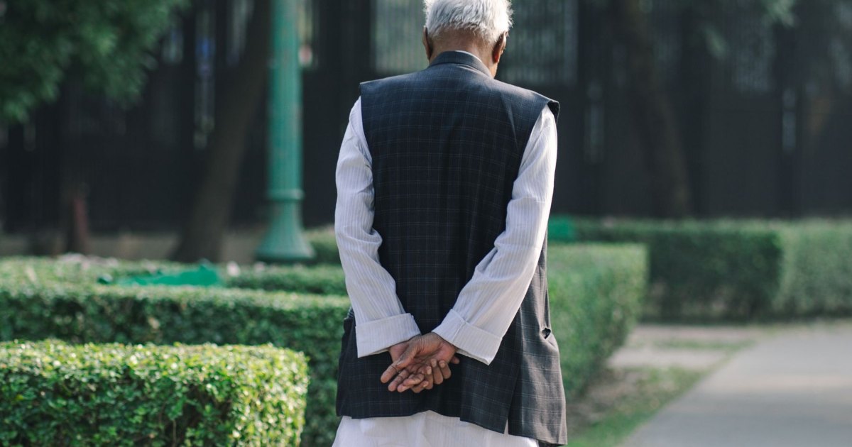 An older man walking away along a garden path, seen from behind