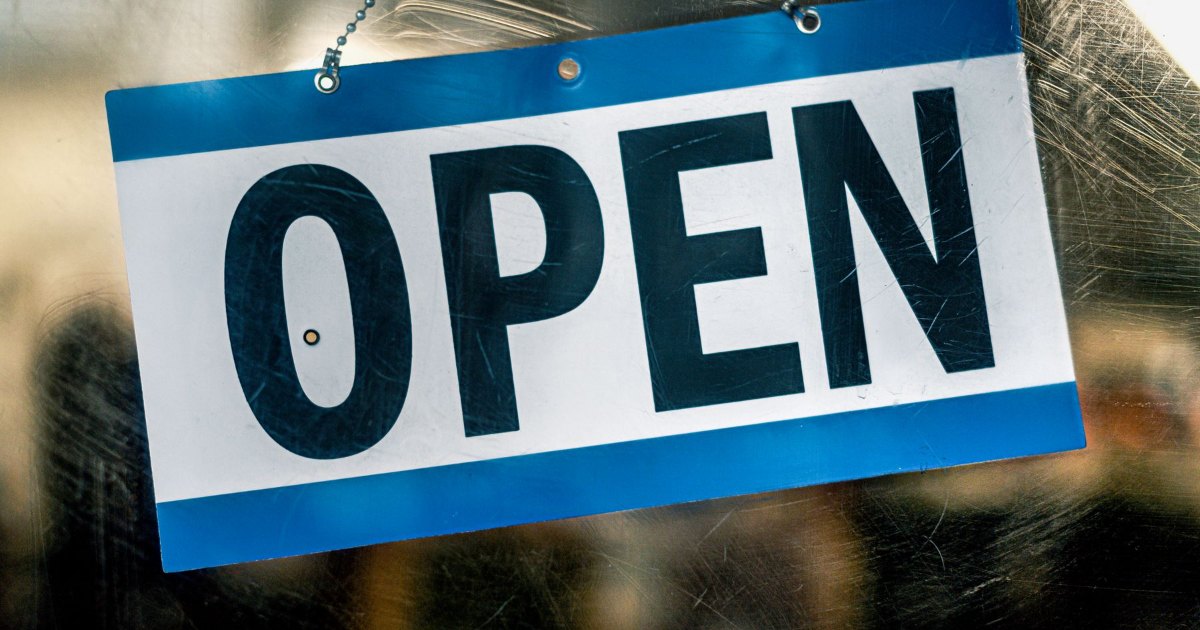 Open sign on a shop door A blue and white open sign hanging on the glass door of a retail shop
