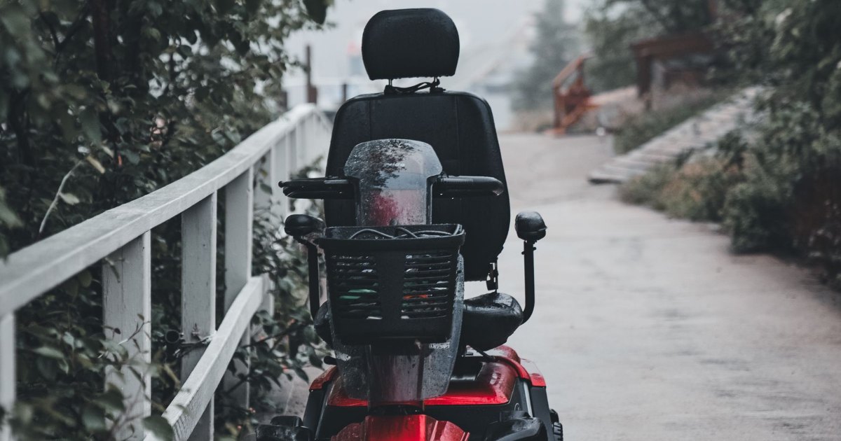 A mobility scooter being ridden along a paved path, seen from behind