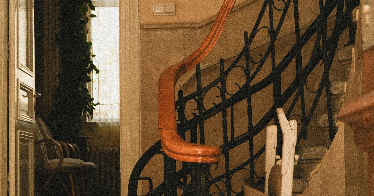 A stairlift rail and chair fitted along the side of a staircase with iron banisters