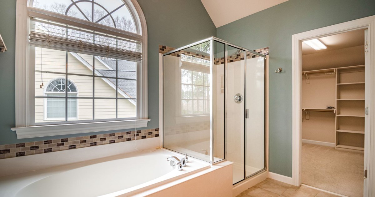 A white bath and glass shower enclosure below an arched bathroom window