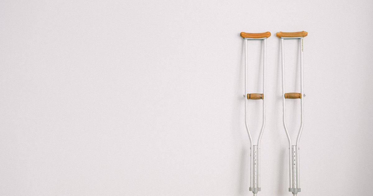 A pair of wooden underarm crutches standing against a plain wall