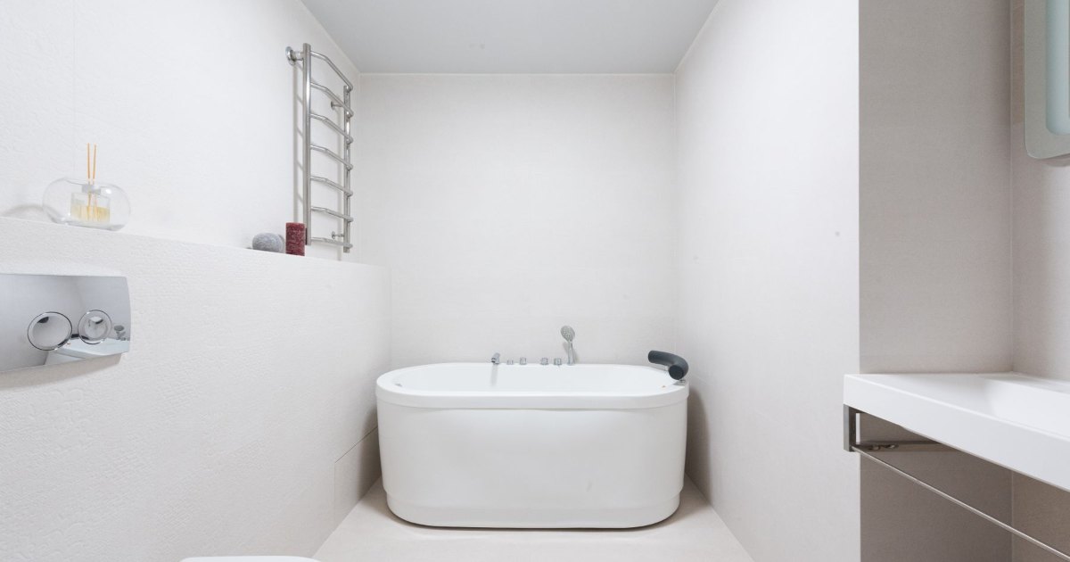A white oval bath in a plain white bathroom with a window