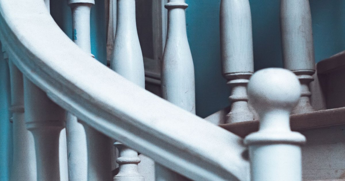 Close view of pale painted spindles and a rounded handrail on a staircase