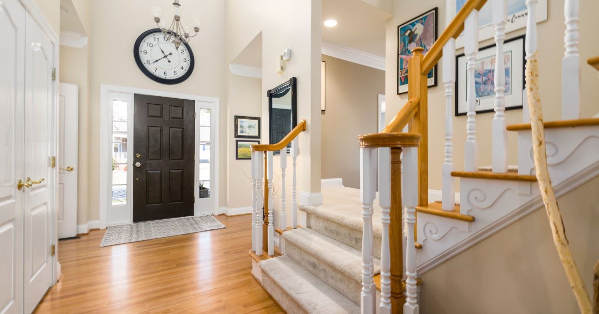 A bright hallway with a wooden staircase, console table and wall clock