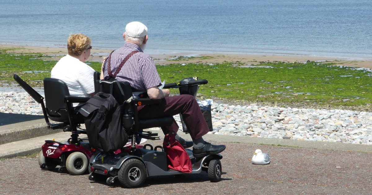 Mobility scooters on a seafront Two people riding mobility scooters along a seafront path, seen from behind