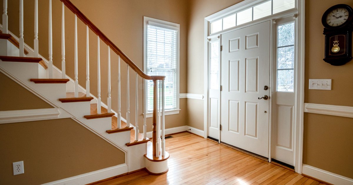A staircase with white spindles in a bright entrance hall with wood flooring