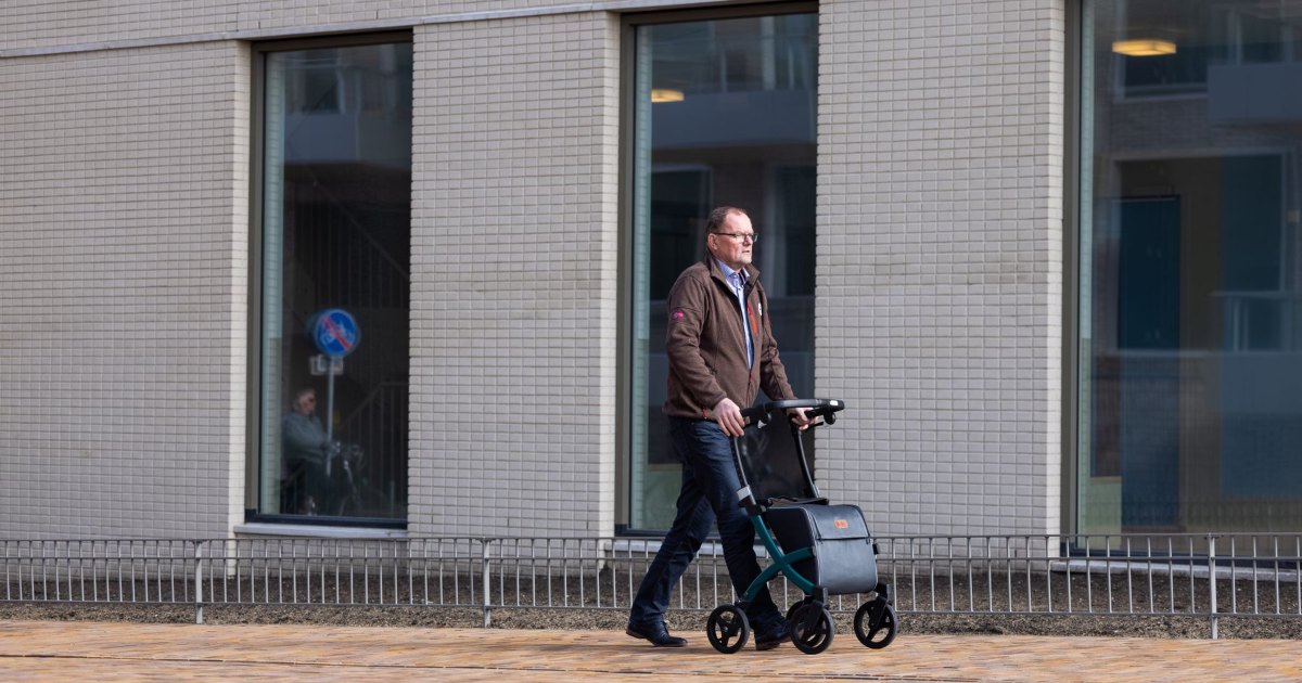 A person using a rollator walker on a pavement beside a building