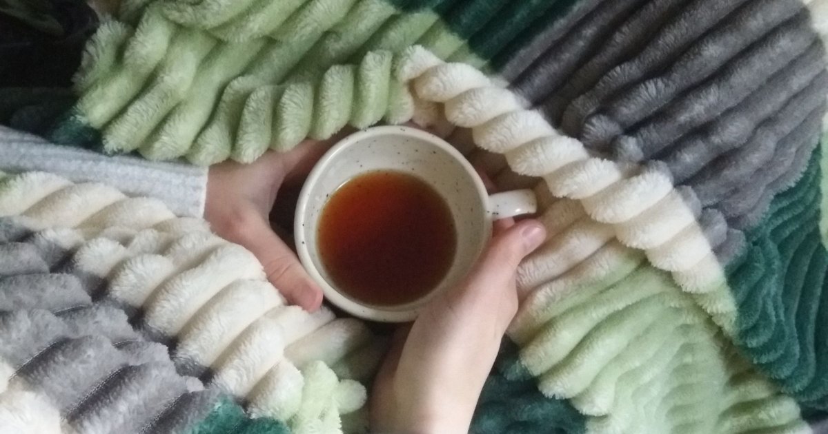 A close view of hands holding a mug over a knitted blanket