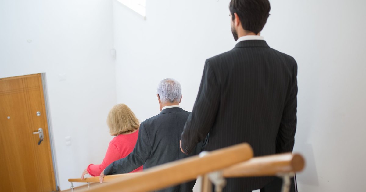 An older couple sitting on a staircase talking with a man in a suit, as at a home stairlift survey visit