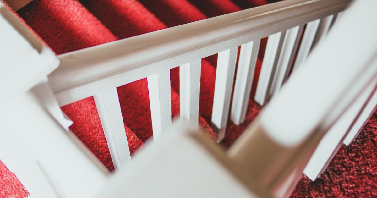 A staircase with a red carpet runner and a white painted balustrade