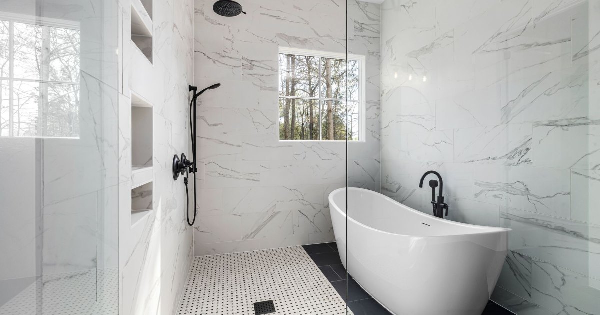 A bright marble bathroom with a freestanding bath and black taps