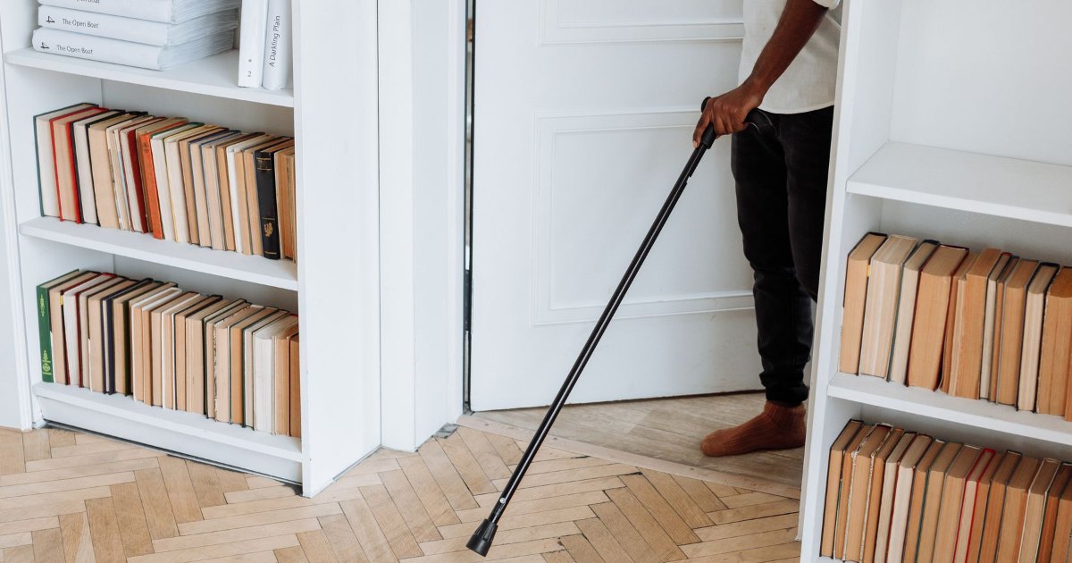 Walking cane by a bookcase A walking cane resting against a white bookcase at home