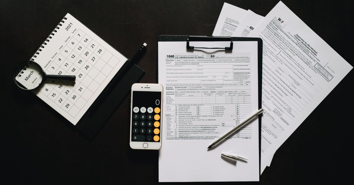 Tax forms, a calculator and a pen laid out flat on a desk