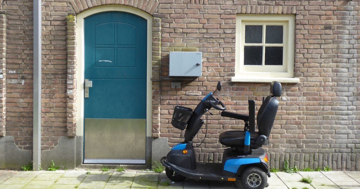 A blue four wheeled mobility scooter parked beside a brick wall and front door