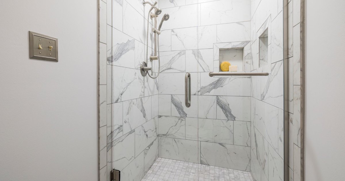 A marble tiled shower enclosure with a built in shelf