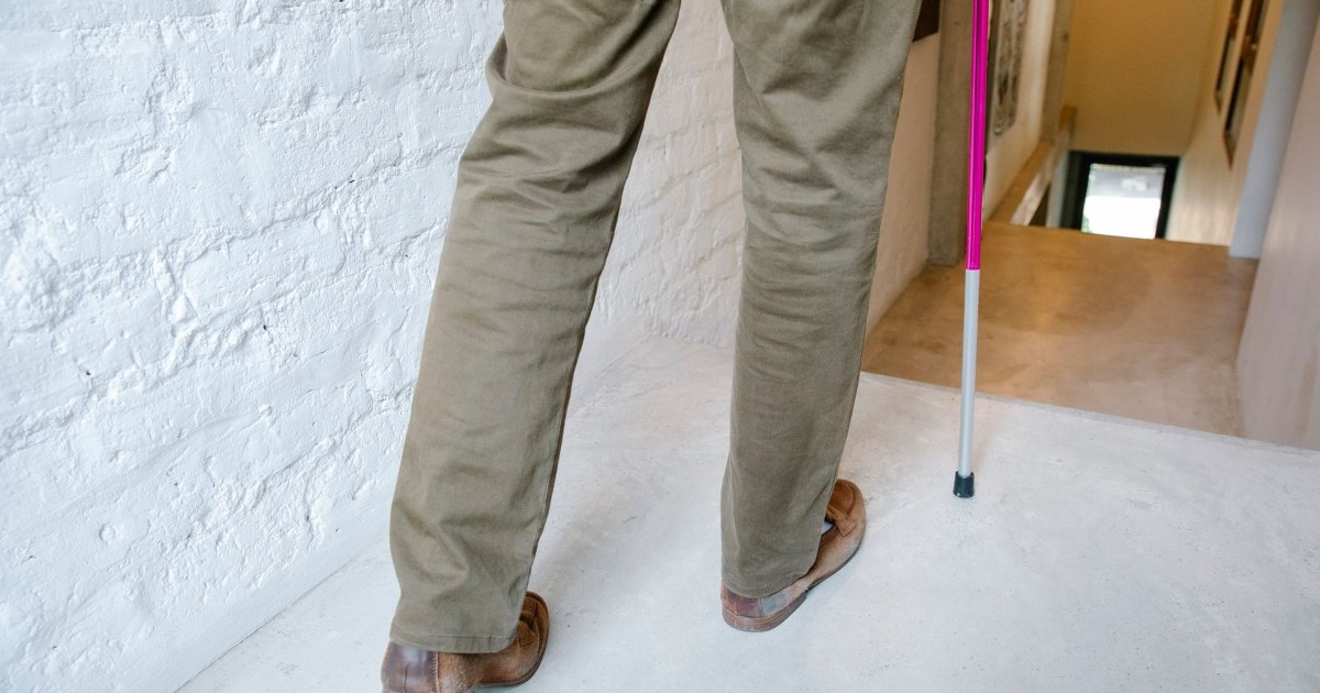 A close view of a person's legs and the tip of a walking cane indoors