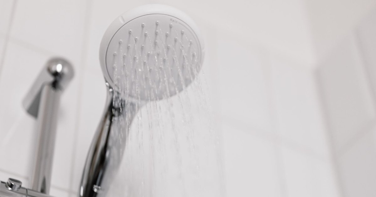 A close view of a chrome hand held shower head against white tiling