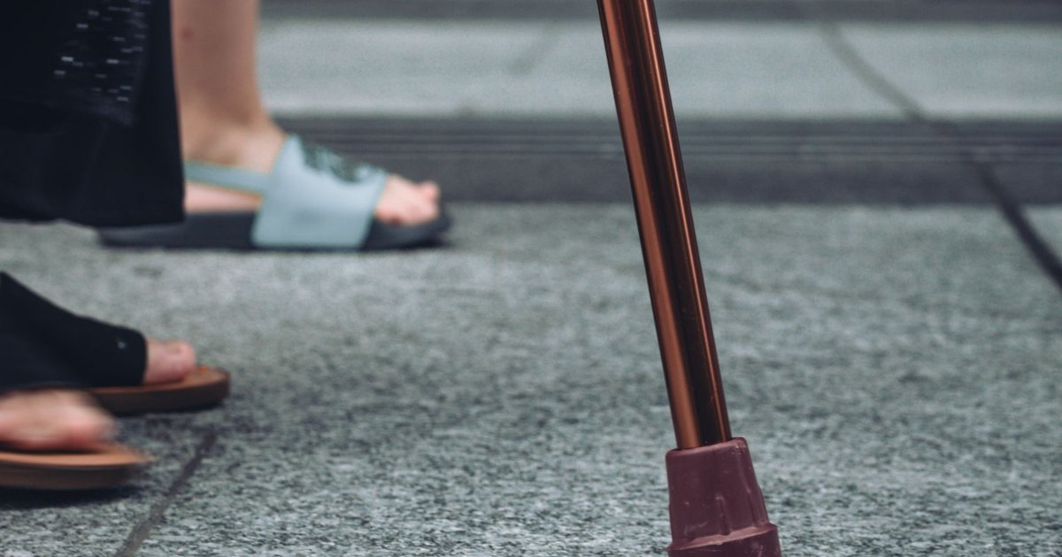A close view of feet in sandals beside the tip of a walking stick