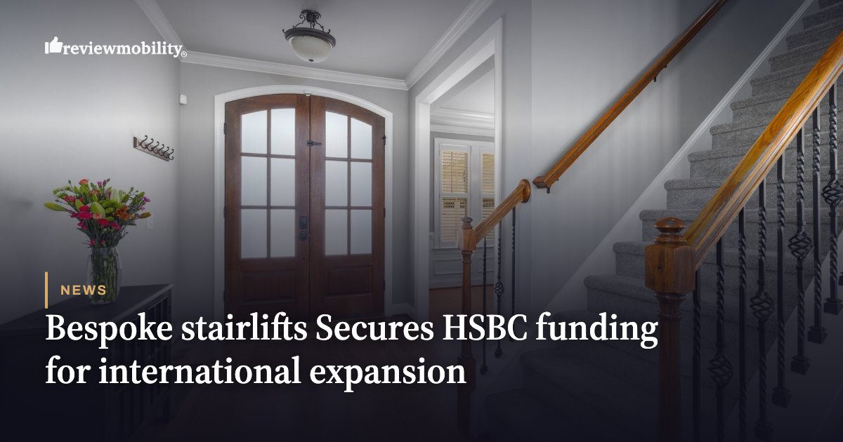 Indoor home entry with a wooden front door and a curved staircase, used as the hero image for a Review Mobility news article on stairlift funding.