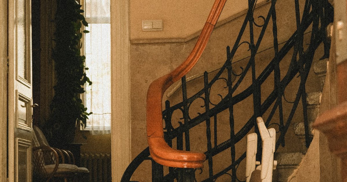 Stairlift companies to avoid Curved staircase with an ornate banister and a stairlift seat and rail fitted along the stairs.