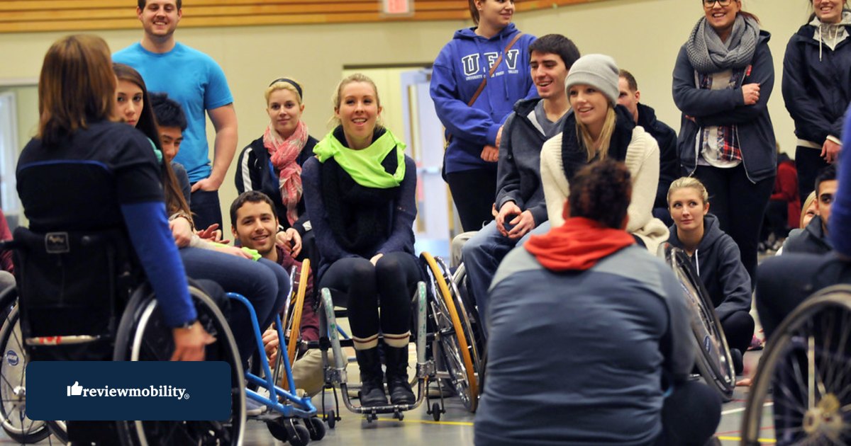 A group of wheelchair users gathered in a sports hall listening to a coach.